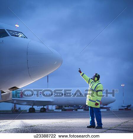 Airport worker guiding aircraft on runway at night View Large Photo Image Stock Image - Airport worker guiding aircraft on runway at night. Fotosearch