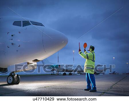 Airport worker guiding aircraft on runway at night View Large Photo Image Stock Photo - Airport worker guiding aircraft on runway at night. Fotosearch