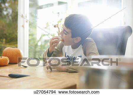 Picture - Boy eating pumpkin soup in kitchen. Fotosearch