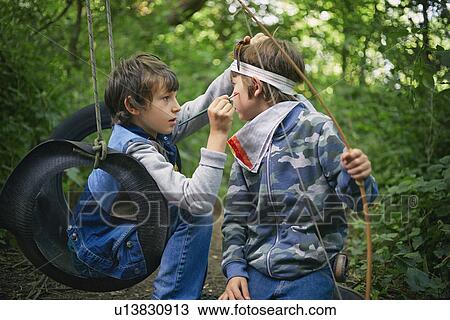 Boy face painting friend whilst playing in forest View Large Photo Image Stock Image - Boy face painting friend whilst playing in forest. Fotosearch