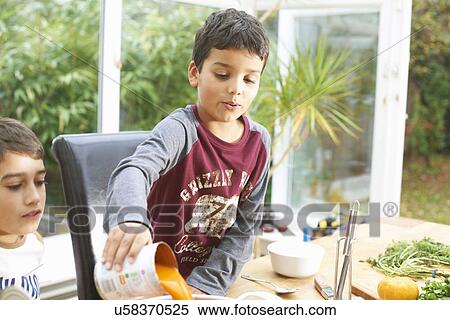 Stock Photography - Boy pouring tin of tomato soup into saucepan. Fotosearch