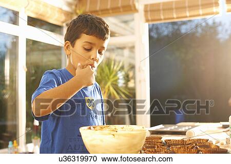 Stock Image - Boy tasting cake mixture in kitchen. Fotosearch