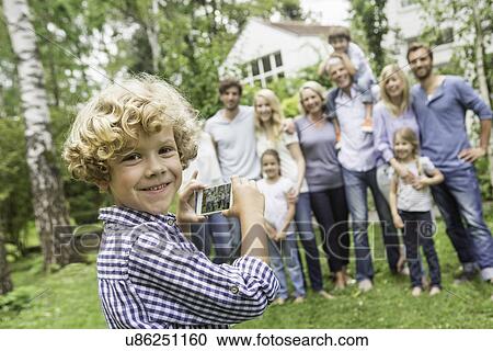 Boy using smartphone with family in background View Large Photo Image Stock Image - Boy using smartphone with family in background. Fotosearch