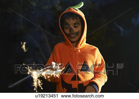 Stock Image - Boy wearing halloween pumpkin costume with sparkler in garden at night. Fotosearch