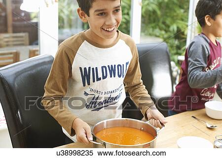 Stock Photography - Boys at kitchen table holding pan of tomato soup. Fotosearch