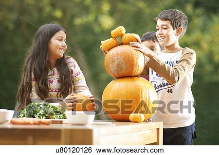 Stock Photograph - Brothers and sister in garden balancing pumpkins. Fotosearch
