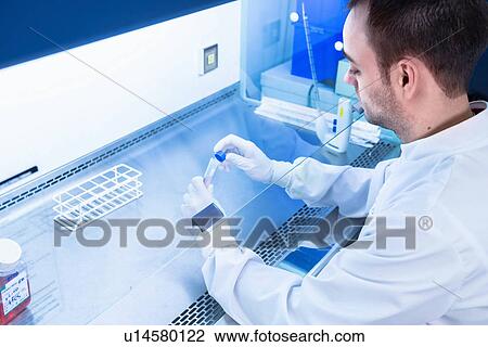 Stock Image - "Cancer research laboratory, over shoulder view of scientist preparing cells for centrifuge". Fotosearch