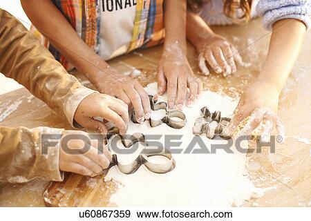 Stock Photo - Children cutting shapes into dough in kitchen. Fotosearch