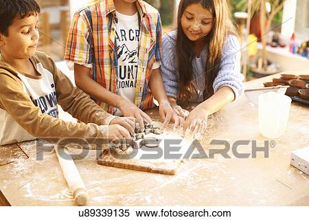 Stock Photography - Children cutting shapes into dough in kitchen. Fotosearch