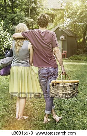 Stock Photo - Couple carrying cushions and picnic basket in garden. Fotosearch