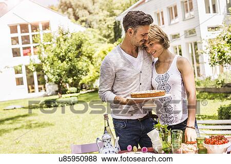 Stock Photo - "Couple in garden having tender moment, man holding cake". Fotosearch