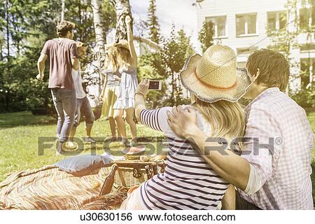 Couple taking photo of friends dancing in garden View Large Photo Image Stock Photograph - Couple taking photo of friends dancing in garden. Fotosearch