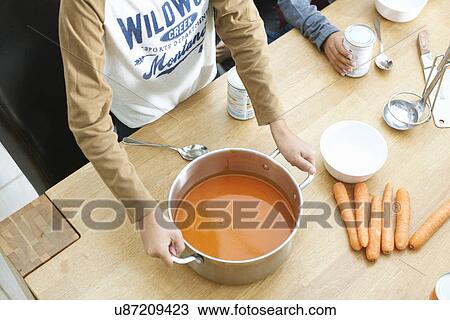 Stock Image - Cropped shot of boys at kitchen table holding pan of tomato soup. Fotosearch