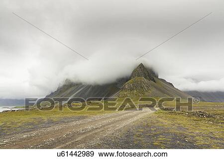 Stock Photo - "Dirt track and low cloud over mountains, Hvalnes, Iceland, ". Fotosearch
