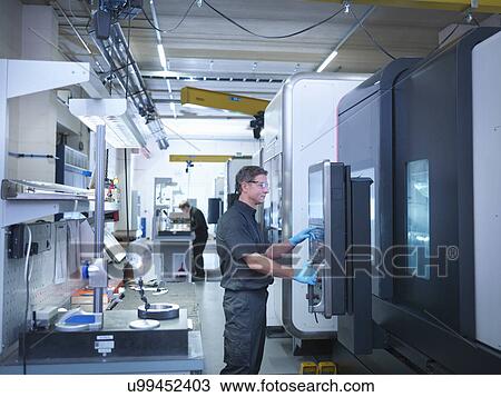 Stock Image - Engineer at CNC machine in engineering factory. Fotosearch