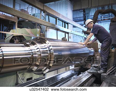 Stock Image - Engineer at lathe in engineering factory. Fotosearch