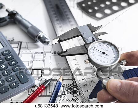 Engineer holding dial caliper with measurement equipment sitting on technical drawing View Large Photo Image Stock Photo - Engineer holding dial caliper with measurement equipment sitting on technical drawing. Fotosearch