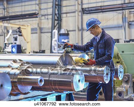Stock Image - Engineer inspecting finished steel rollers in engineering factory. Fotosearch