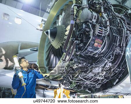 Stock Image - Engineer inspecting jet engine in aircraft maintenance factory. Fotosearch
