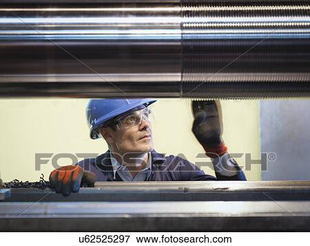 Stock Photo - Engineer inspecting turned steel in engineering factory. Fotosearch