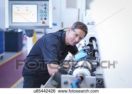 Stock Photograph - Engineer setting up honing machine in factory. Fotosearch