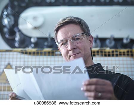 Stock Photograph - Engineer with plans in front of CNC machine in factory. Fotosearch