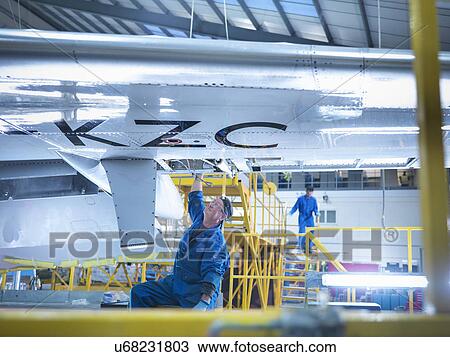 Stock Image - Engineer working on aircraft wing in aircraft maintenance factory. Fotosearch