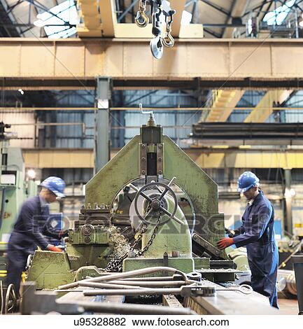Stock Image - Engineers at lathe in engineering factory. Fotosearch