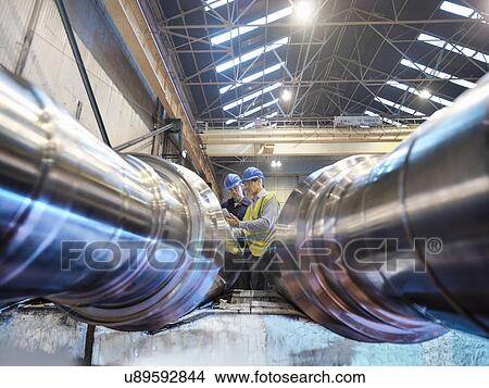 Picture - "Engineers inspecting finished steel rollers in engineering factory, low angle view". Fotosearch