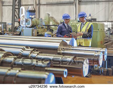 Stock Photograph - Engineers inspecting finished steel rollers in engineering factory. Fotosearch