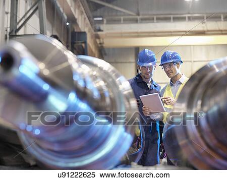 Stock Photography - Engineers inspecting finished steel rollers in engineering factory. Fotosearch