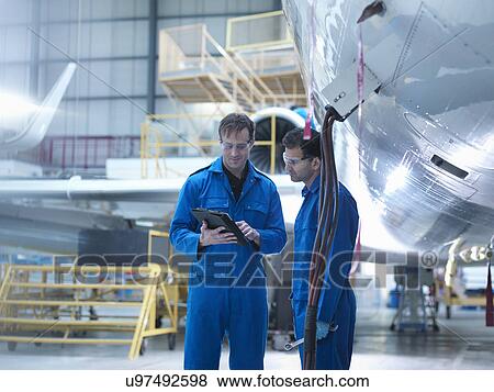 Stock Photo - Engineers using digital tablet and in discussion in aircraft maintenance factory. Fotosearch