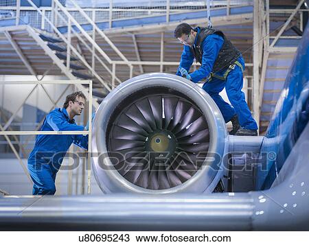 Stock Image - Engineers working on aircraft engine in aircraft maintenance factory. Fotosearch