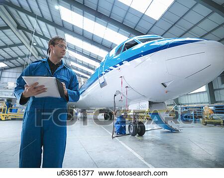 Stock Photo - Engineers working on aircraft in aircraft maintenance factory. Fotosearch