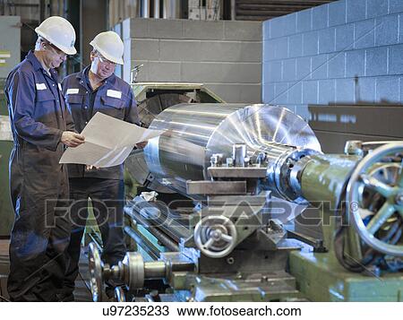 Stock Image - Engineers working with drawings on lathe. Fotosearch