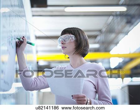 Stock Photograph - Female worker writing on whiteboard in factory. Fotosearch