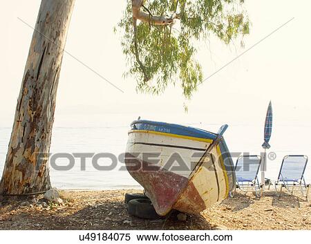 Stock Photography - "Fishing boat and empty deck chairs on beach, Corfu, Greece". Fotosearch