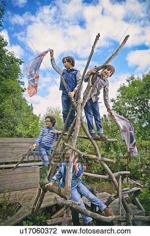 Stock Image - Four boys climbing on homemade climbing frame in garden. Fotosearch