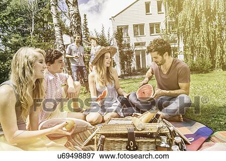 Stock Photo - "Friends having picnic in garden, man slicing watermelon". Fotosearch