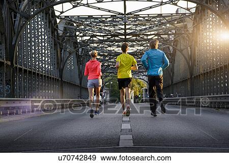 Stock Photo - "Friends jogging on bridge, Munich, Bavaria, Germany". Fotosearch