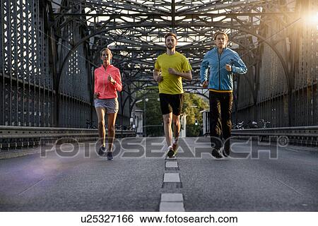 Stock Photograph - "Friends jogging on bridge, Munich, Bavaria, Germany". Fotosearch