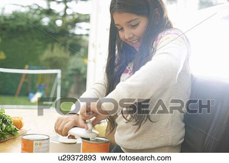 Stock Image - Girl at kitchen table opening can of tomato soup. Fotosearch
