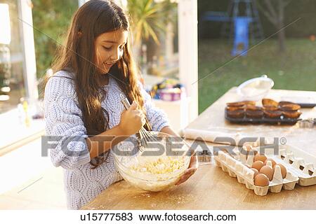 Stock Image - Girl beating mixture in bowl in kitchen. Fotosearch