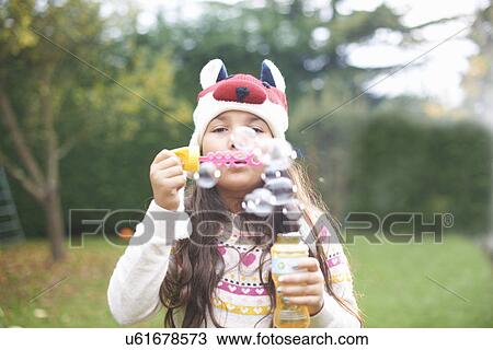 Stock Image - Girl blowing bubbles in garden. Fotosearch