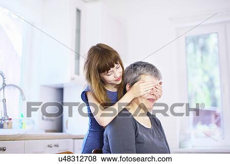Girl covering grandmothers eyes at kitchen table View Large Photo Image Stock Photo - Girl covering grandmothers eyes at kitchen table. Fotosearch