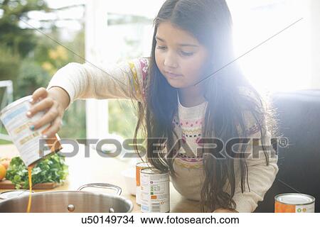 Picture - Girl pouring tin of tomato soup into saucepan. Fotosearch