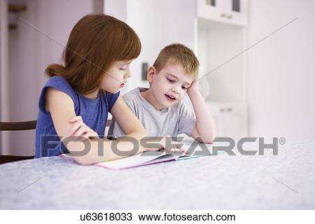 Girl reading book with brother at kitchen table View Large Photo Image Stock Image - Girl reading book with brother at kitchen table. Fotosearch