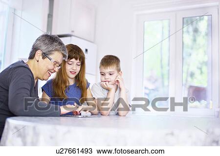Grandmother and grandchildren using digital tablet at kitchen table View Large Photo Image Stock Image - Grandmother and grandchildren using digital tablet at kitchen table. Fotosearch