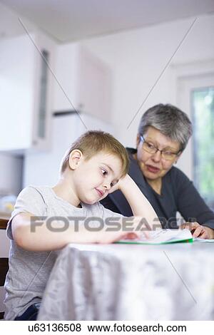 Grandmother reading book with bored grandson at kitchen table View Large Photo Image Stock Photo - Grandmother reading book with bored grandson at kitchen table. Fotosearch