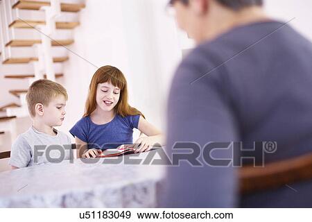 Grandmother watching grandchildren read book at kitchen table View Large Photo Image Stock Photo - Grandmother watching grandchildren read book at kitchen table. Fotosearch